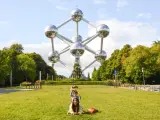 Familia posa frente al Atomium, un icono de que ver en Bruselas. Un niño salta detrás de su madre en el césped.