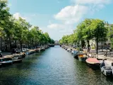Canal de Ámsterdam con barcos, árboles y edificios bajo un cielo azul con nubes.