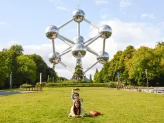 Familia posa frente al Atomium, un icono de que ver en Bruselas. Un niño salta detrás de su madre en el césped.