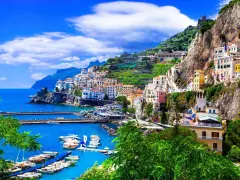 Un pueblo costero italiano con casas coloridas en laderas verdes, un puerto con barcos y el mar azul. ¡Un destino perfecto donde viajar en junio!