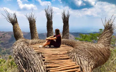 Mujer sentada en una mano gigante de ramas, disfrutando de la vista. Un lugar perfecto para viajar a Java, Indonesia.