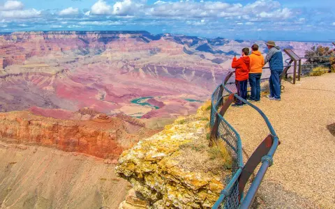 Tres personas admiran la inmensidad del cañón del Colorado, con sus capas rocosas de tonos rojizos y un río turquesa serpenteando en el fondo.
