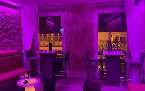 Ambiente moderno y acogedor para comer en Coruña. Mesas altas, taburetes y sofás rojos bajo luces violetas.