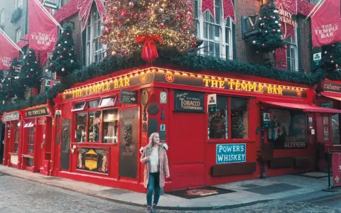 Una mujer pasea por la calle empedrada frente al icónico pub The Temple Bar en Dublín, decorado para Navidad. ¡Una excelente idea de qué hacer en Dublín!