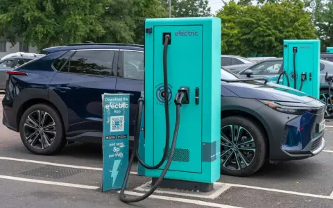 Coches eléctricos cargando. Las ventajas y desventajas de los coches eléctricos se reflejan en esta escena de carga, con un cartel que invita a descargar una app para ahorrar.