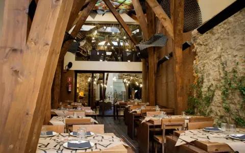 Mesas puestas en un restaurante rústico con vigas de madera y paredes de piedra, ideal para comer en Avilés.