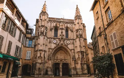 Fachada de una iglesia gótica con detalles ornamentados y dos torres. A los lados, edificios antiguos de piedra y fachadas de color claro. Un lugar que ver en Avignon.