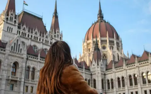 Mujer con abrigo de pelo admira el Parlamento de Budapest, un destino ideal donde viajar en noviembre en Europa.
