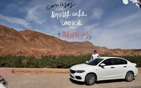 Consejos para alquilar coche y conducir en Marruecos. Paisaje desértico con palmeras y una mujer junto a un coche blanco.