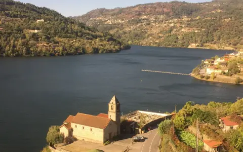 Un pueblo pintoresco a orillas de un río, con una iglesia y un cementerio. Las colinas verdes y las casas se extienden hasta donde alcanza la vista. ¡Un lugar ideal para ir a toro!