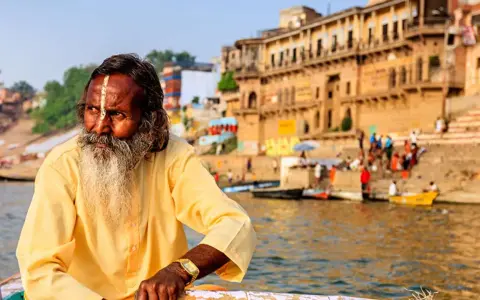Un hombre con barba y marca en la frente navega en el Ganges, una escena típica al viajar a la India.