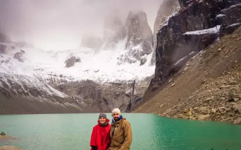 Pareja posa frente a un lago turquesa y montañas nevadas, un paisaje imperdible que ver en Chile.