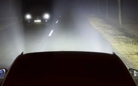 Luces de carretera o largas iluminan la noche, revelando un coche adelante y el camino.