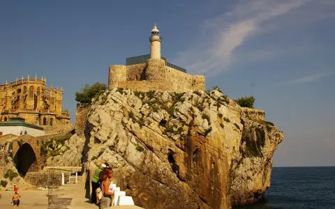 Descubre qué ver en Castro Urdiales: un faro en un castillo sobre rocas, con una iglesia gótica al fondo y gente paseando.