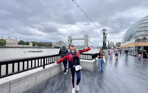 Mujer sonriente con brazos extendidos en Londres, con la Torre de Londres y el Tower Bridge al fondo. ¡Excelentes consejos para viajar a Londres!