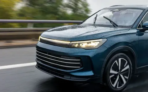 Un elegante coche seminuevo de color azul oscuro circula por una carretera mojada, con las luces encendidas.