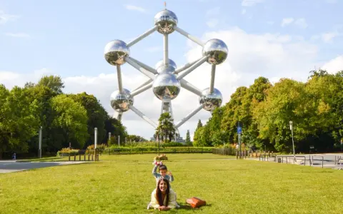 Familia posa frente al Atomium, un icono de que ver en Bruselas. Un niño salta detrás de su madre en el césped.
