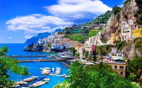 Un pueblo costero italiano con casas coloridas en laderas verdes, un puerto con barcos y el mar azul. ¡Un destino perfecto donde viajar en junio!