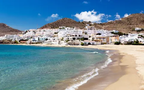 Pueblo blanco a orillas del mar turquesa, ideal para descubrir qué ver en Cabo de Gata. Playas doradas y casas encaladas bajo un cielo azul.