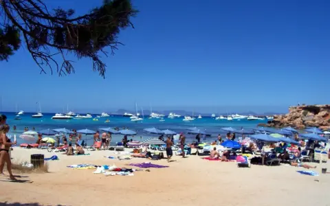Playa con gente, sombrillas y barcos en el mar azul. Un día perfecto para ver qué ver en Formentera.