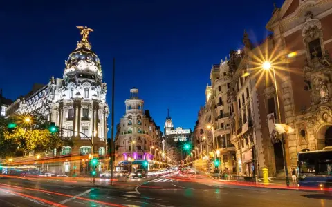 Noche vibrante en Madrid, con edificios iluminados y estelas de luz de coches. ¡Un fin de semana en Madrid inolvidable!