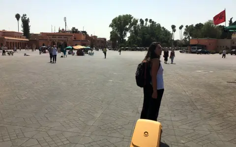 Una mujer con mochila y maleta amarilla en una plaza de Marruecos. Piensa en qué llevar a Marruecos para este viaje.