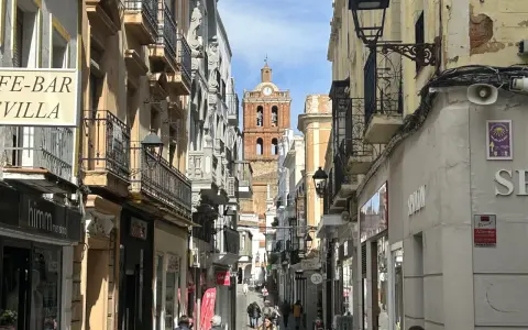 Calle comercial con edificios antiguos y un campanario al fondo. Descubre qué ver en Zafra y disfruta de su encanto.