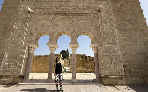 Mujer posa ante arcos de Medina Azahara. Se puede visitar Medina Azahara por libre, explorando su rica historia y arquitectura.