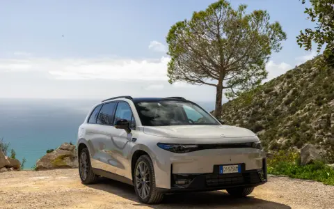 Un SUV blanco moderno, uno de los tipos de coches eléctricos, aparcado en un camino de tierra con el mar y una colina verde de fondo.