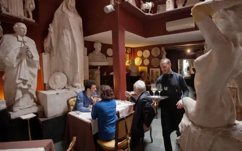 Un camarero sirve copas de vino en un restaurante único, rodeado de esculturas. Un lugar ideal donde comer en Roma.
