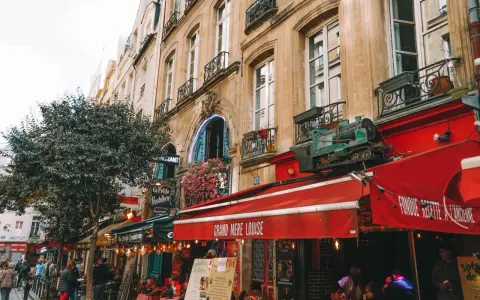 Calle parisina con restaurantes y mesas al aire libre, ideal para comer barato en París. Un tren decorativo adorna un toldo rojo.