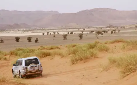 Un todoterreno blanco avanza por dunas de arena en un paisaje desértico de Marruecos. ¡Una aventura de Marruecos 5 días!