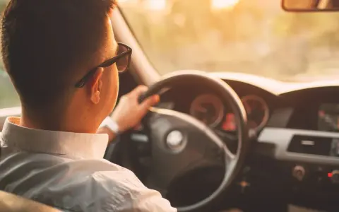 Hombre con gafas de sol conduce al atardecer. ¡Cuidado con la velocidad, te pueden multar!
