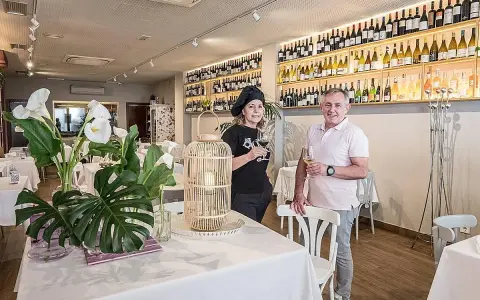 Pareja sonriente en un restaurante con estanterías llenas de vino. Un lugar ideal para saber donde comer en Logroño.