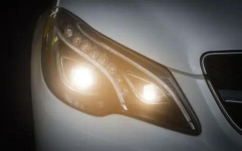 Primer plano de un faro de coche moderno con luces cortas encendidas, un símbolo de visibilidad y seguridad en la carretera.