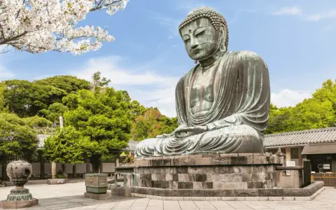 El Gran Buda de bronce, una maravilla que ver en Kamakura, sentado serenamente bajo cerezos en flor y rodeado de exuberante vegetación.