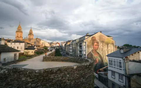 Mural de mujer en edificio, con la muralla romana y la catedral al fondo. Imprescindible que ver en Lugo.