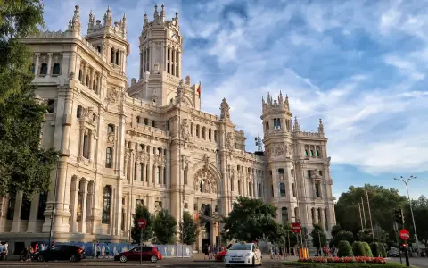 Un día en Madrid: el Palacio de Cibeles, un taxi blanco y coches circulan bajo un cielo azul con nubes.