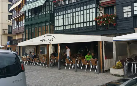 Gente disfrutando de una comida en Lekeitio, sentados en mesas al aire libre bajo un toldo blanco.