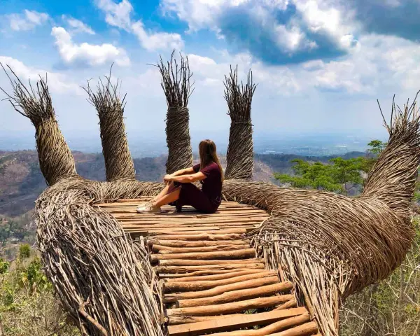 Mujer sentada en una mano gigante de ramas, disfrutando de la vista. Un lugar perfecto para viajar a Java, Indonesia.