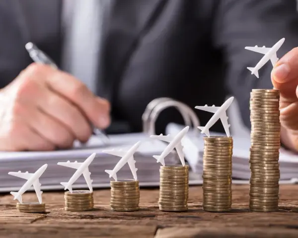 Pequeños aviones sobre pilas de monedas crecientes, simbolizando cómo viajar barato es posible con planificación.