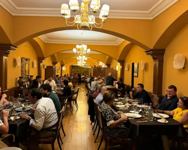 Gente disfrutando de una cena en un elegante restaurante con arcos y lámparas doradas. Una experiencia culinaria memorable para comer en Olite.