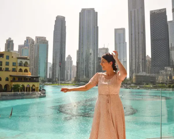 Mujer disfrutando de su viaje a Dubai, con rascacielos y una fuente de agua de fondo.
