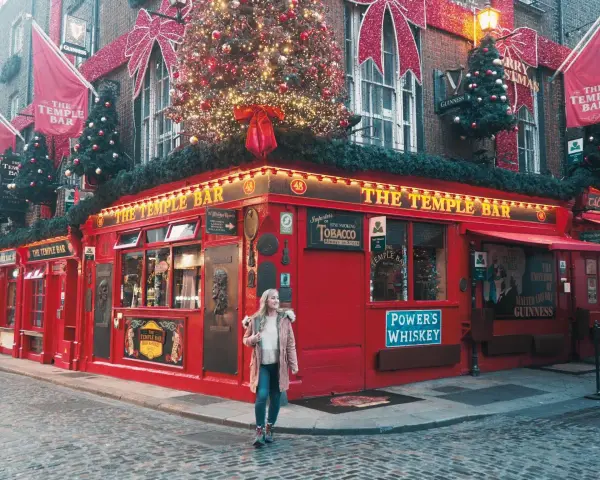 Una mujer pasea por la calle empedrada frente al icónico pub The Temple Bar en Dublín, decorado para Navidad. ¡Una excelente idea de qué hacer en Dublín!