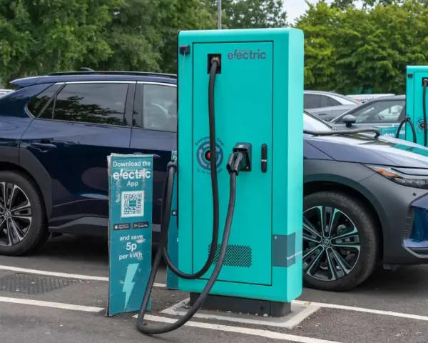 Coches eléctricos cargando. Las ventajas y desventajas de los coches eléctricos se reflejan en esta escena de carga, con un cartel que invita a descargar una app para ahorrar.
