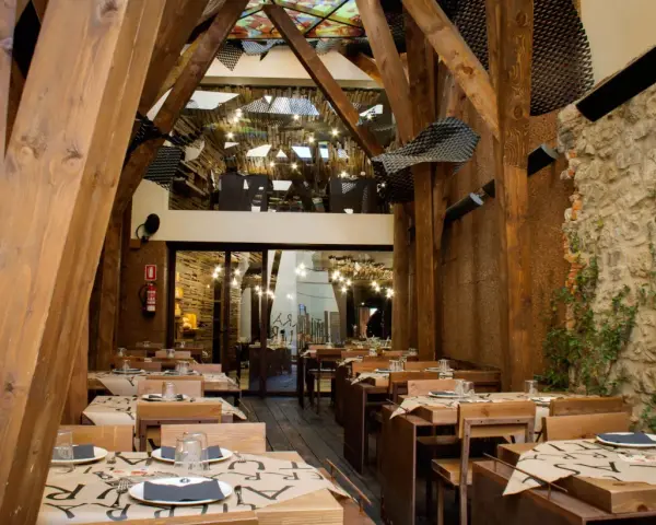 Mesas puestas en un restaurante rústico con vigas de madera y paredes de piedra, ideal para comer en Avilés.