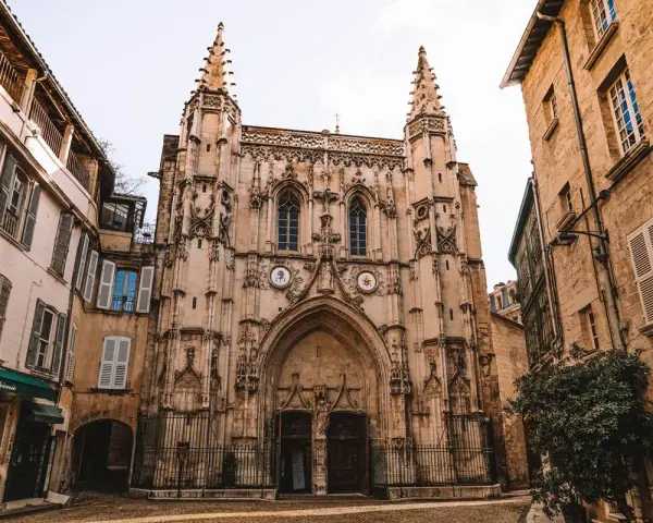 Fachada de una iglesia gótica con detalles ornamentados y dos torres. A los lados, edificios antiguos de piedra y fachadas de color claro. Un lugar que ver en Avignon.