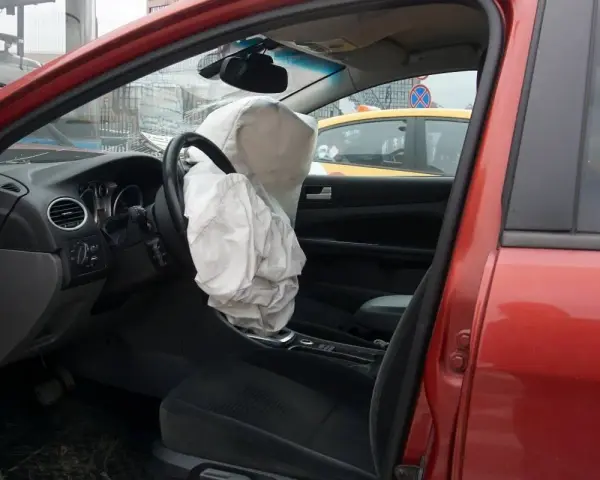 Interior de coche rojo con airbag del conductor desplegado, indicando la dirección del vehículo activa o pasiva tras un impacto.