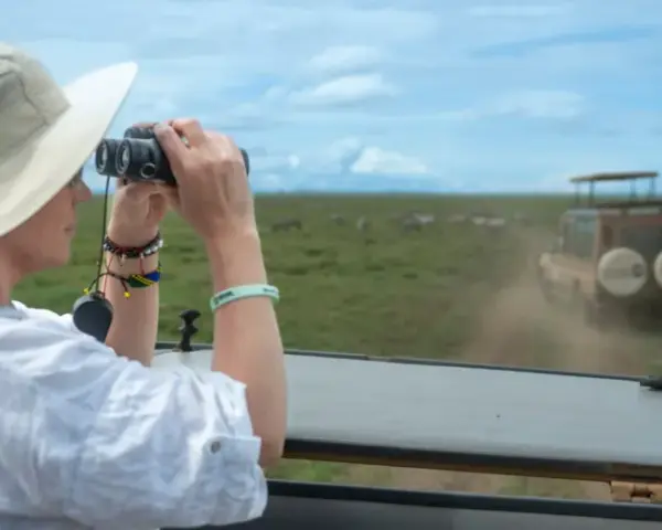 Mujer con sombrero y binoculares observa cebras en la sabana, disfrutando de su viaje a Tanzania.