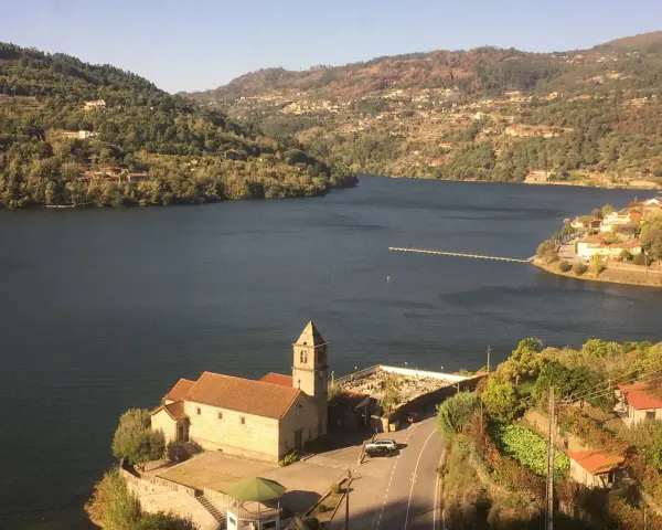 Un pueblo pintoresco a orillas de un río, con una iglesia y un cementerio. Las colinas verdes y las casas se extienden hasta donde alcanza la vista. ¡Un lugar ideal para ir a toro!
